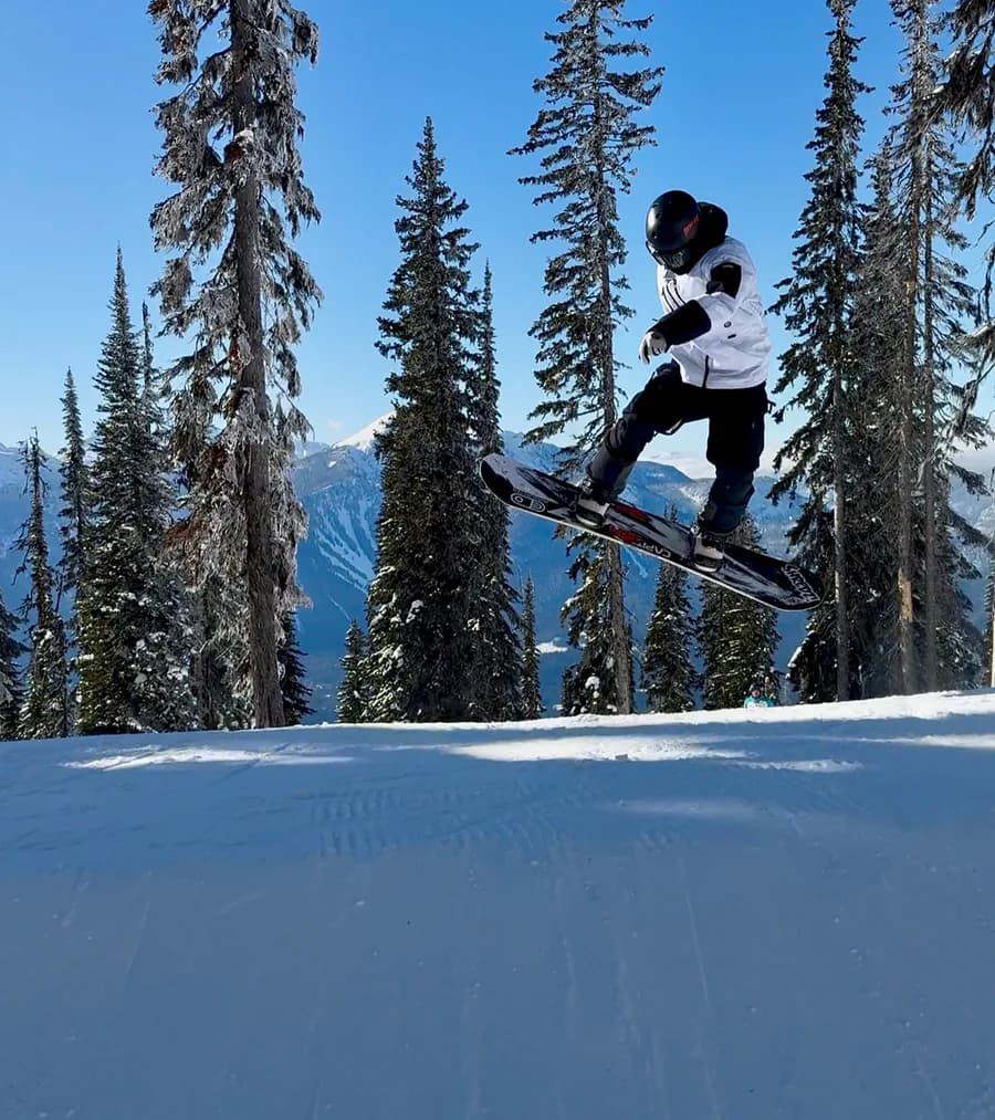 A snowboarder jumping between snow-covered trees at Revelstoke